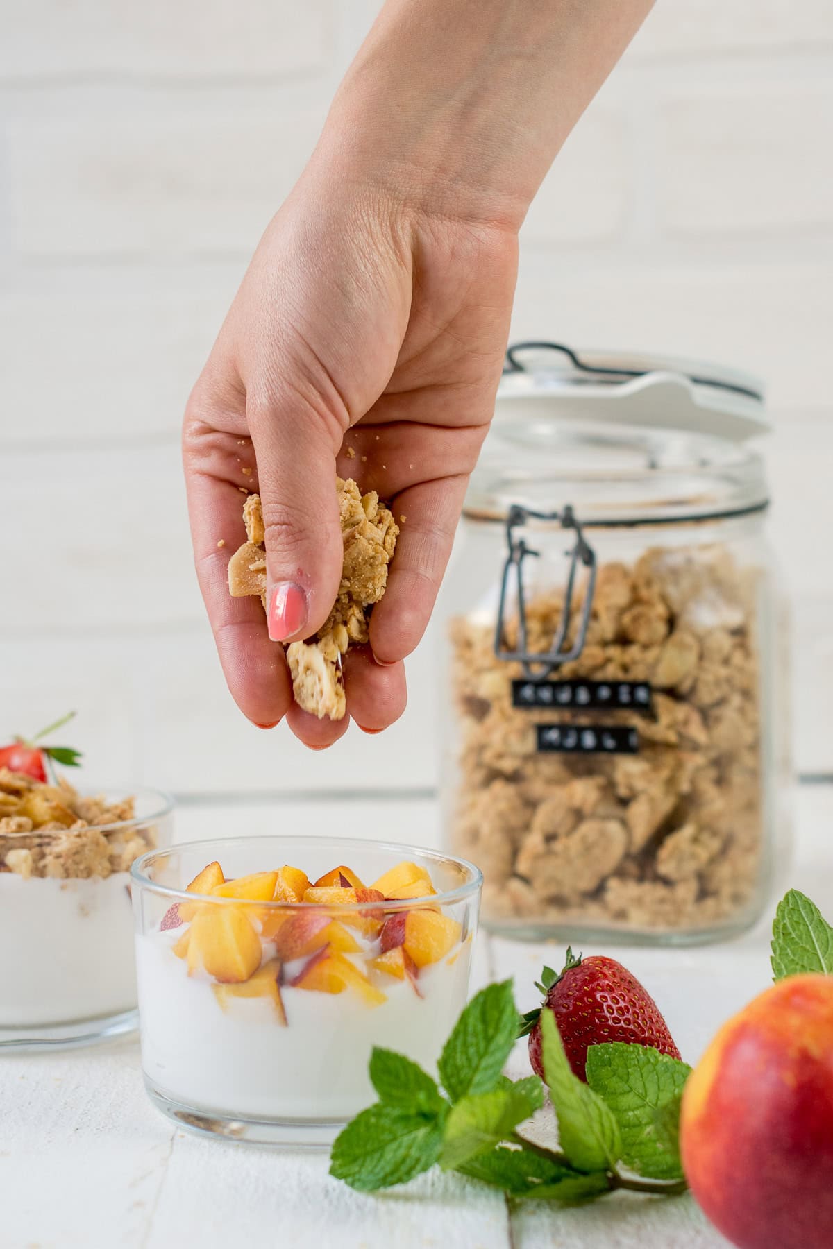 Glas mit Joghurt und Früchten und einer Hand die Knuspermüsli festhält.