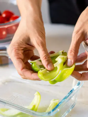 Hände, die grüne Paprika vorschneiden, um beim Kochen Zeit zu sparen