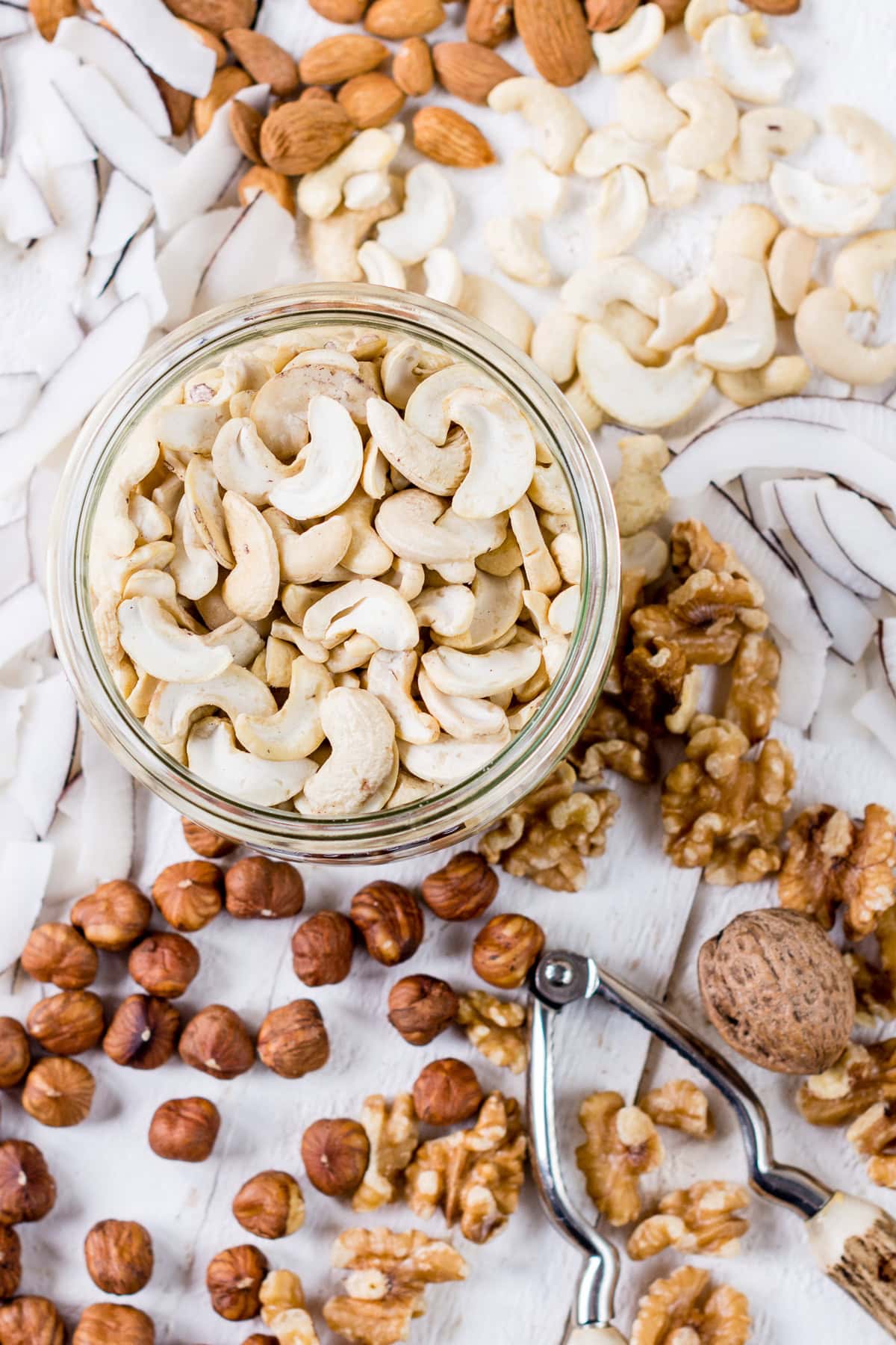 Topshot von einem Glas mit Cashewkernen und anderen Nüssen um das Glas herum.