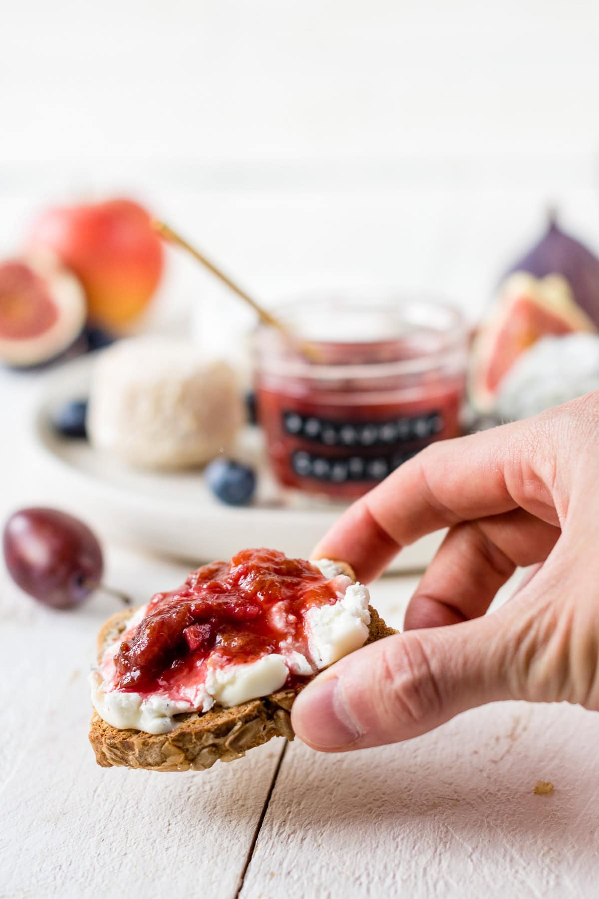 Hand hält ein Stück Brot mit Käse und Zwetschgen Chutney in der Hand.