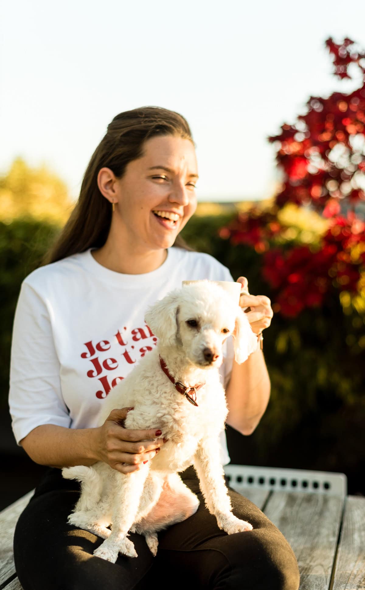 Frau mit Tee in der Hand und Hund auf dem Schoß im Herbst.