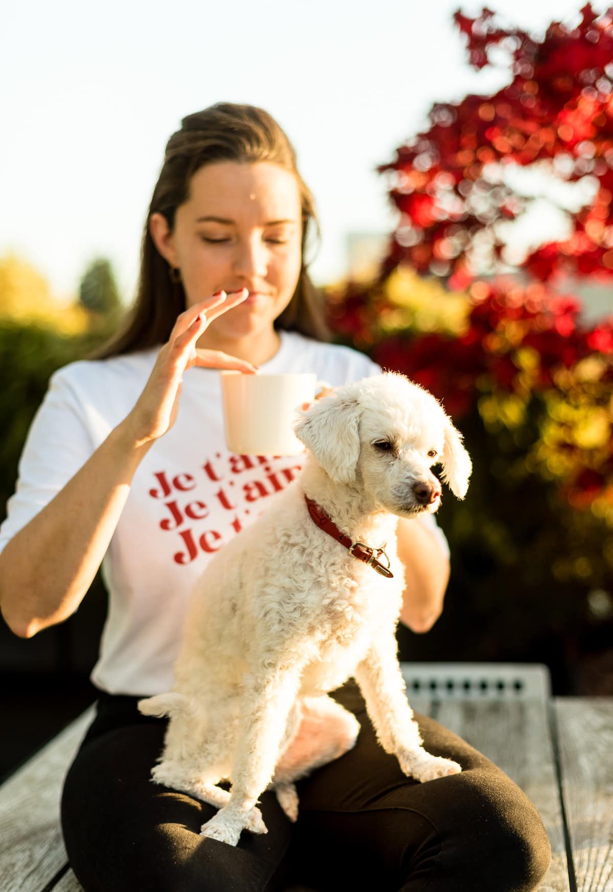 Frau mit Tee in der Hand und Hund auf dem Schoß im Herbst.