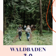 Zwei Frauen laufen einen Waldweg mit Nadelbäumen entlang.