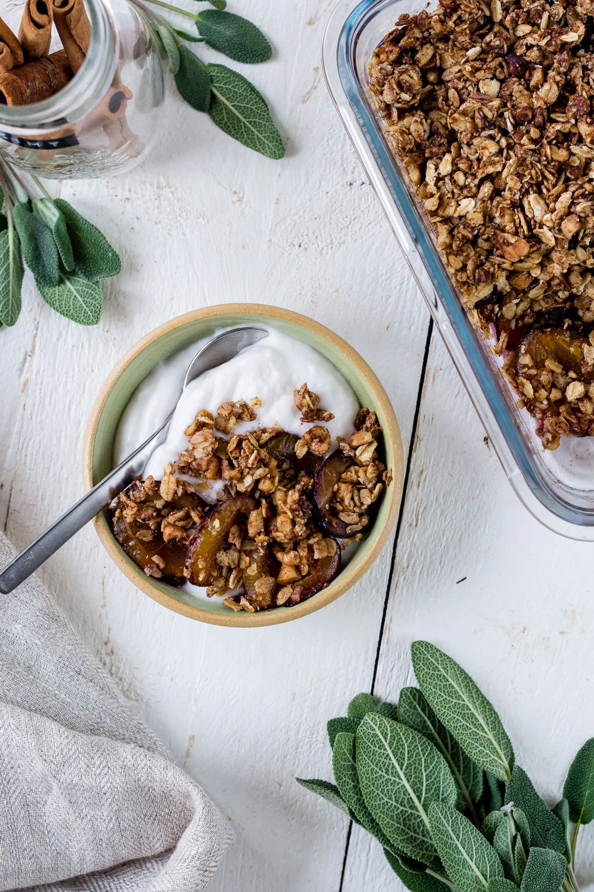 Pinne das Foto um dir das Rezept für gesunden Pflaumen Crumble zu speichern Bild von oben von einer Müslischale und einer Auflaufform mit Joghurt und Pflaumen Crumble.