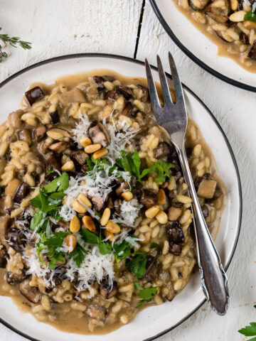 Topshot von einem Teller mit cremigem Pilzrisotto, Kräutern und Parmesan.