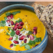 Dunkelblaue Schüssel mit gelber Suppe, garniert mit Granatapfelkernen und Körnerbrot