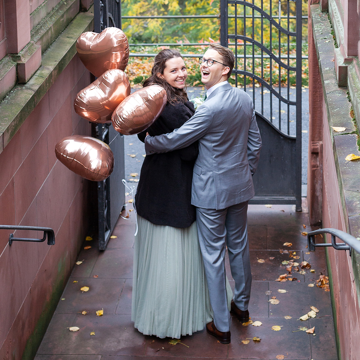 Paar schaut lächelnd in die Kamera und hält Luftballons in Herzform in der Hand.