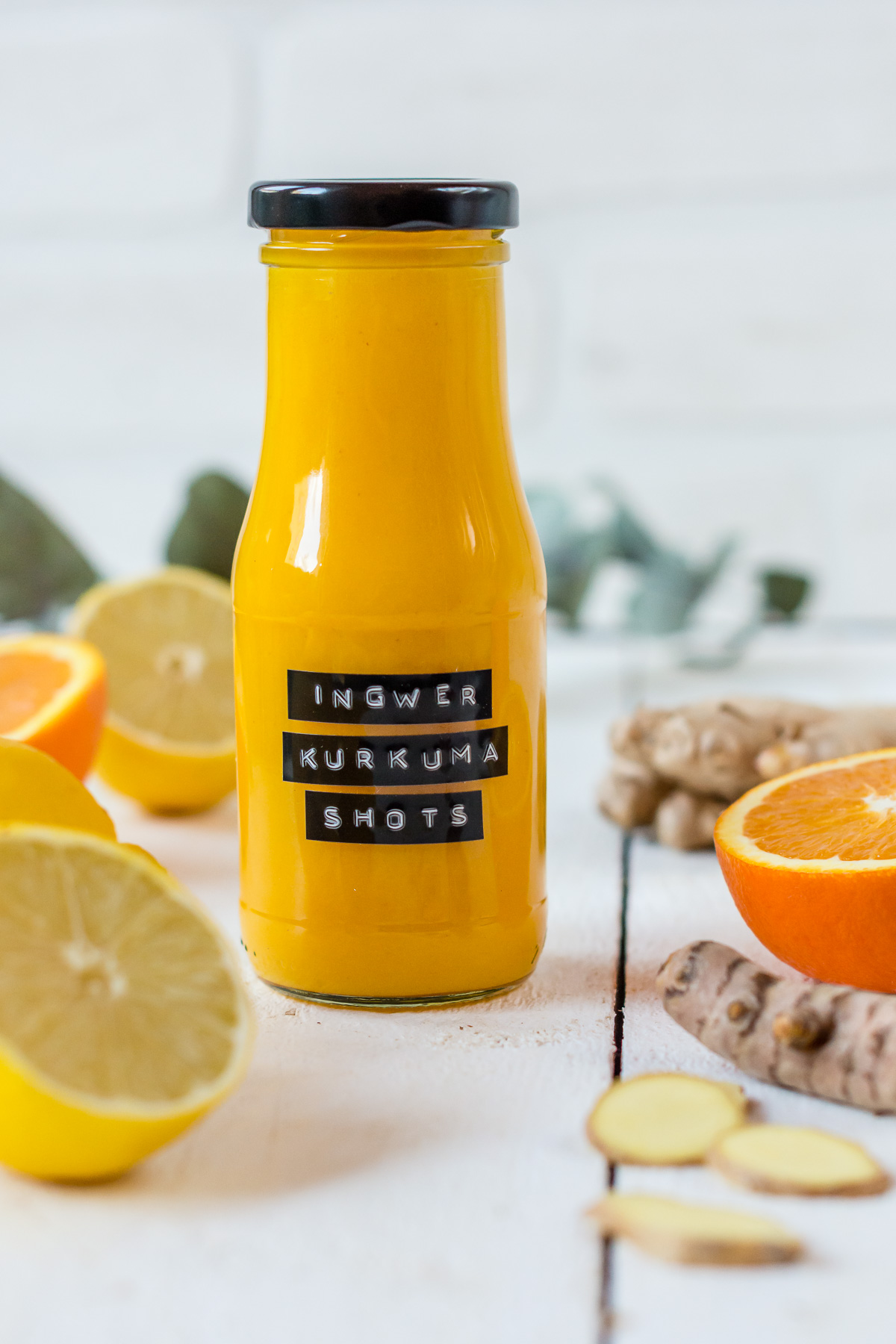 Flasche gefüllt mit Orangen Ingwer Shot und frische Orangen und Ingwer.