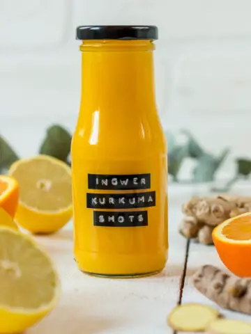 Flasche gefüllt mit Orangen Ingwer Shot und frische Orangen und Ingwer.