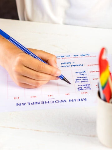 Hand, die einen Stift hält und einen Wochenplan ausfüllt.