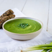 Teller mit grüner Detox Suppe und frischen Kräutern mit zwei Scheiben Brot.