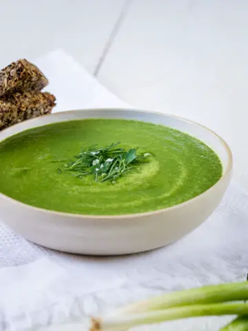 Teller mit grüner Detox Suppe und frischen Kräutern mit zwei Scheiben Brot.