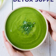 Topshot von zwei Händen die eine Schüssel mit grüner Suppe auf weißem Untergrund hält.