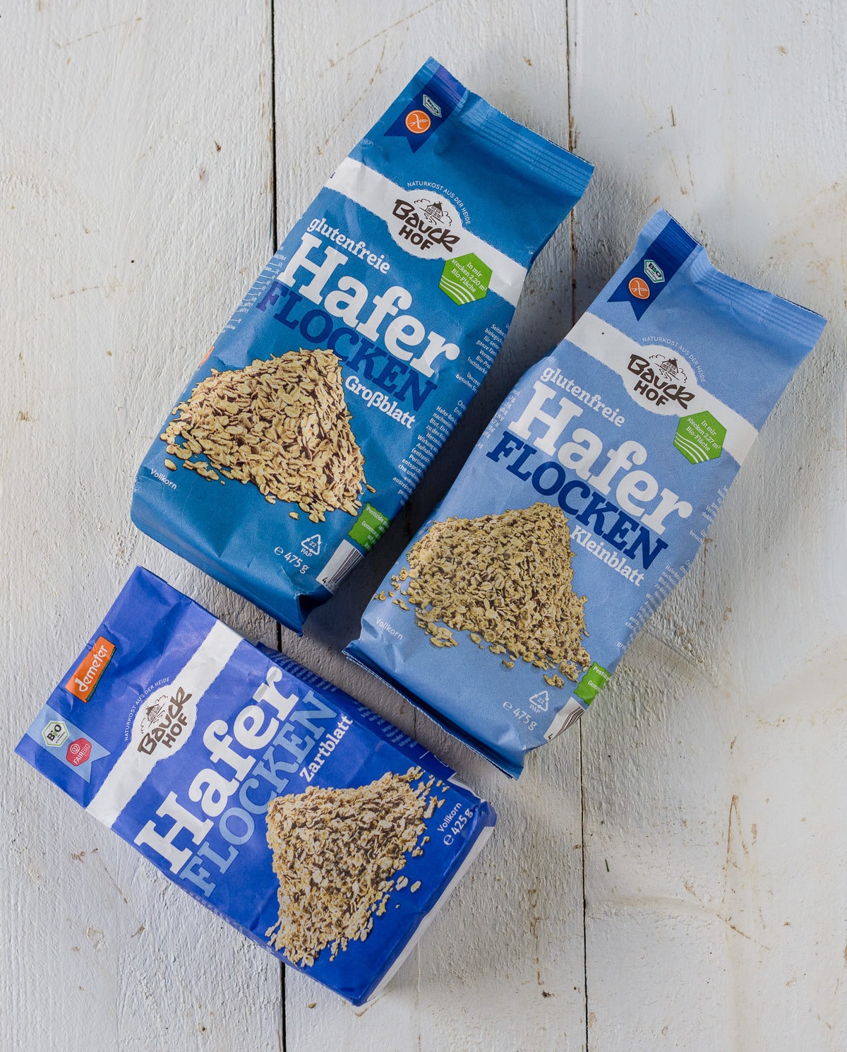 Pinne das Foto, um das Rezept für gesundes Porridge zu speichern! Topshot von verschiedenen Haferflockenverpackungen.