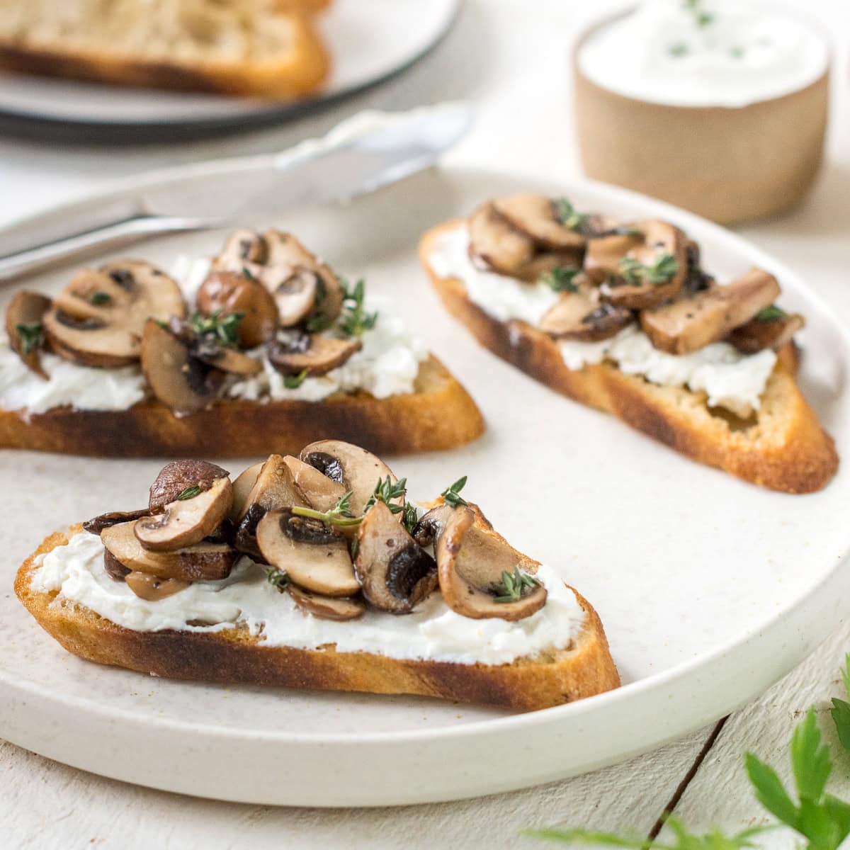 Teller mit drei Bruschetta mit Pilzen und Käse auf weißem Untergrund.