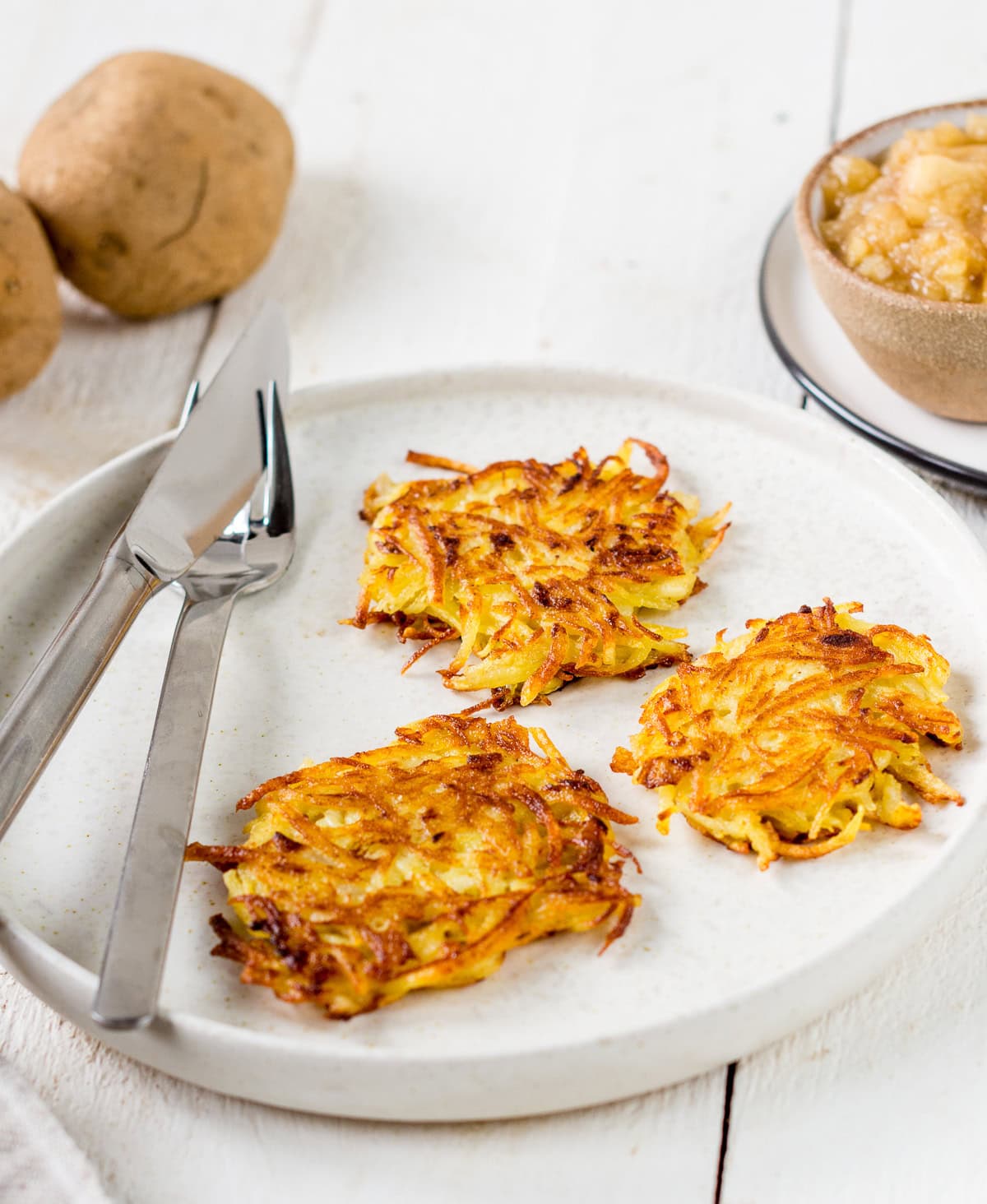 Teller mit Besteck und drei Kartoffelpuffern.