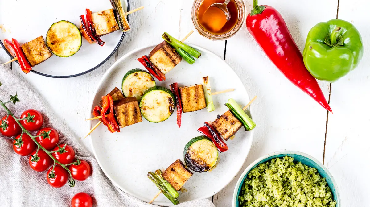 Topshot von zwei Tellern mit veganen Grillspießen mit Tofu und Gemüse.