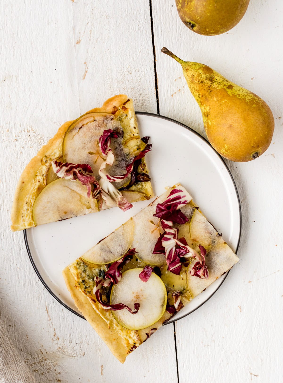 Speichere dieses Foto, um das Rezept für glutenfreien Flammkuchen zu sichern! TOpshot von zwei Stück vegetarischem FLammkuchen mit Birne, Radicchio und Gorgonzola auf einem Teller.