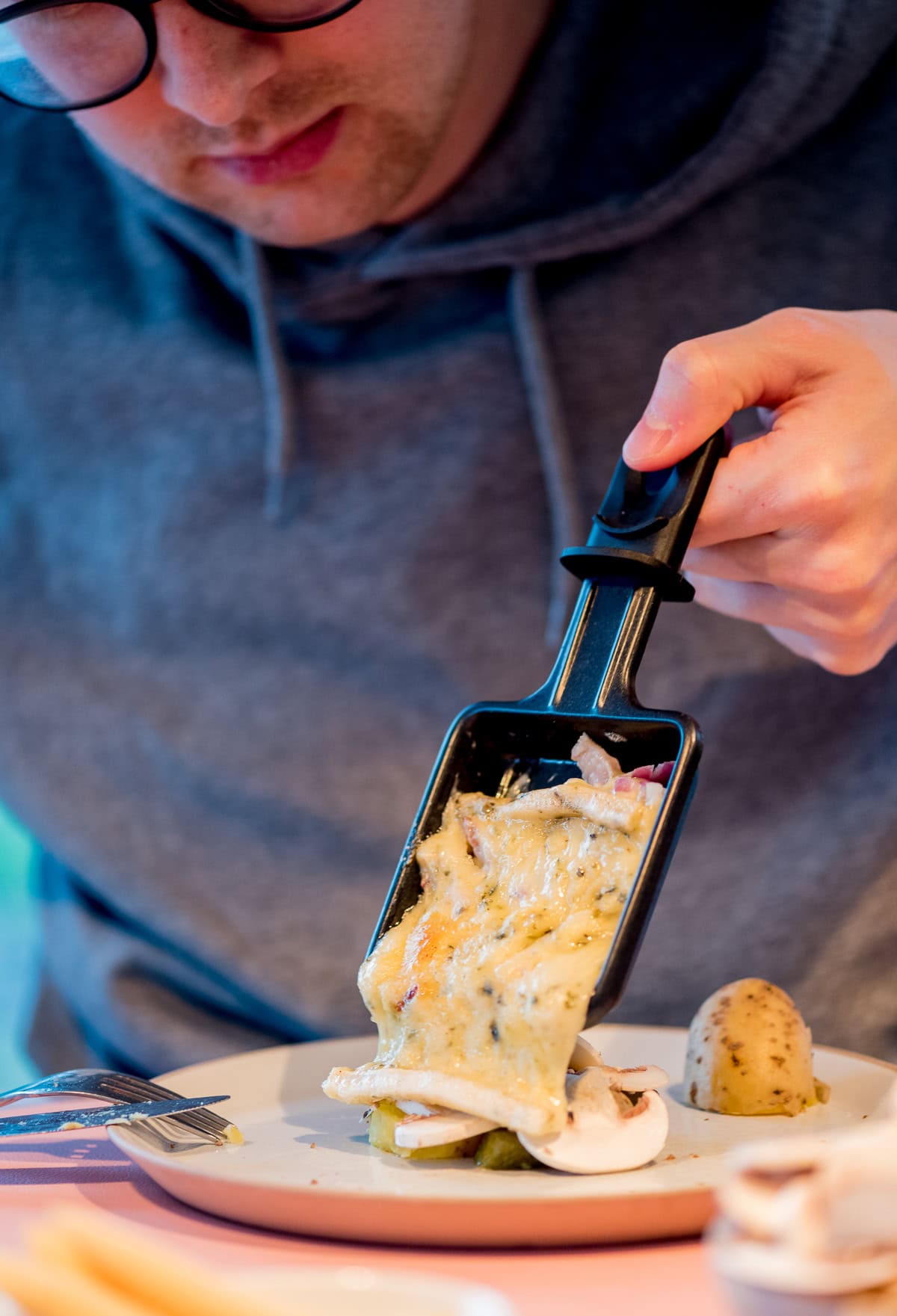Mann lässt geschmolzenen Raclette Käse aus einem Pfännchen auf seinen Teller laufen