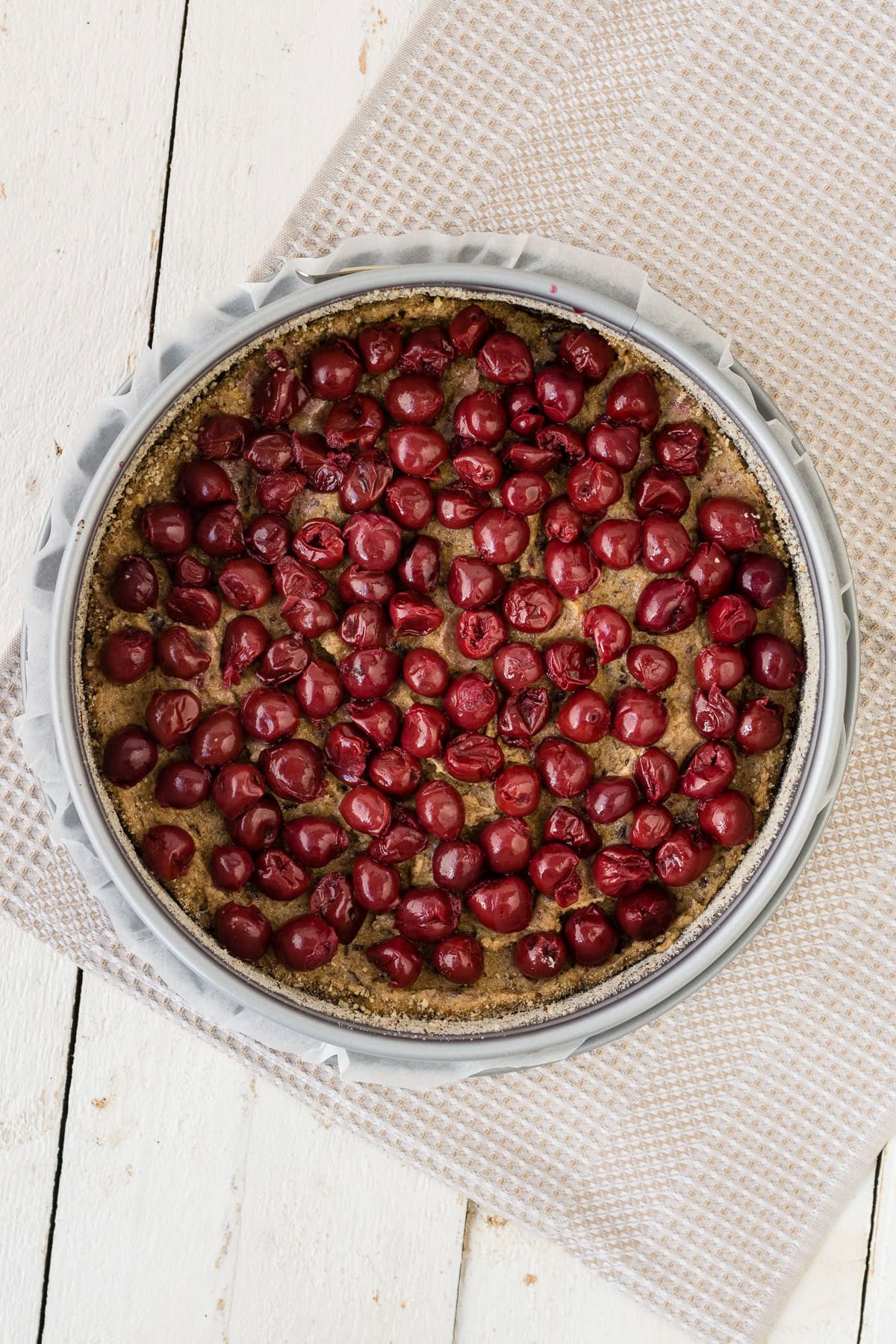 Topshot von ungebackenem Teig mit Kirschen für Schoko-Kirschkuchen auf hellem Untergrund.