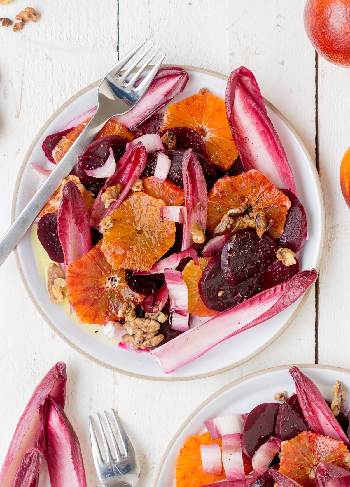 Speichere dieses Foto, um dir das Rezept für diesen Rote Bete Salat zu sichern! Topshot von einem Teller gefüllt mit Salat aus Rote Bete, Blutorange und rotem Chicorée, garniert mit Walnüssen.