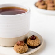 Foto von einer weißen, mit Tee gefüllten Keramiktasse und einer Untertasse auf der zwei Haselnusskekse liegen.