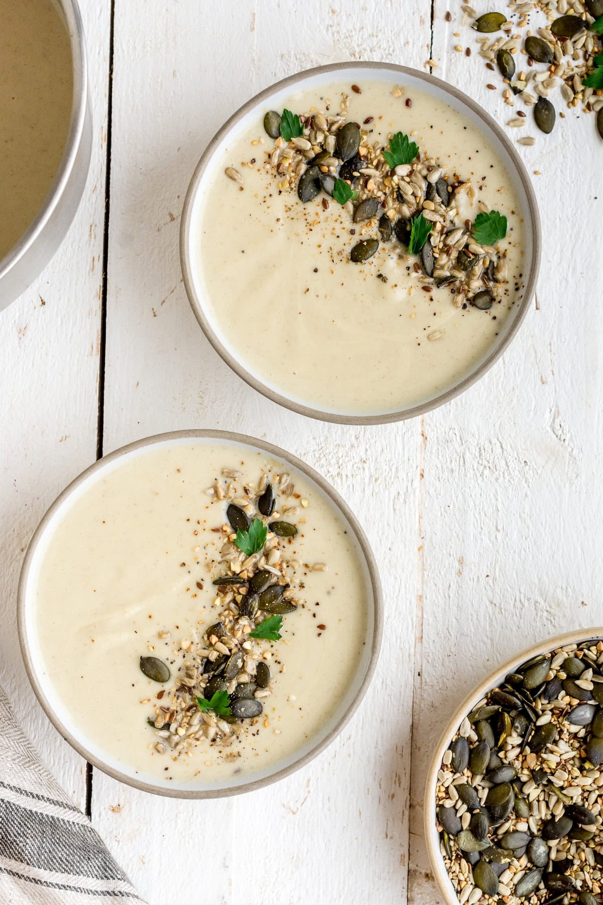 Topshot von zwei Schüsseln Topinambursuppe mit gerösteten Kernen auf weißem Untergrund.