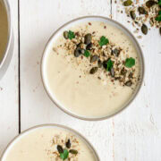 Topshot von zwei Schüsseln Topinambursuppe mit gerösteten Kernen auf weißem Untergrund.