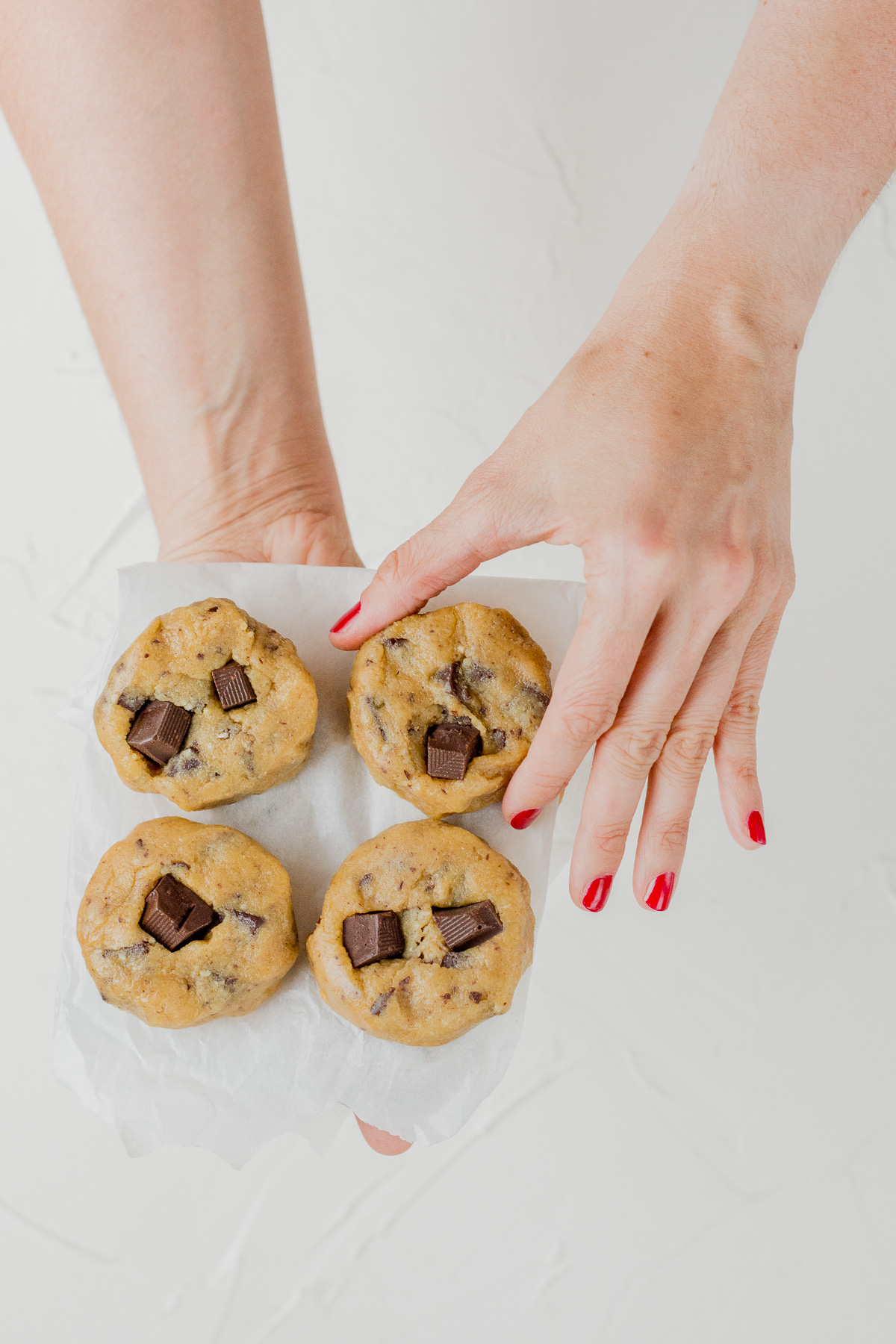 Topshot von Chocolate Chip Cookies, die von zwei Händen vor einem weißen Hintergrund gehalten werden.