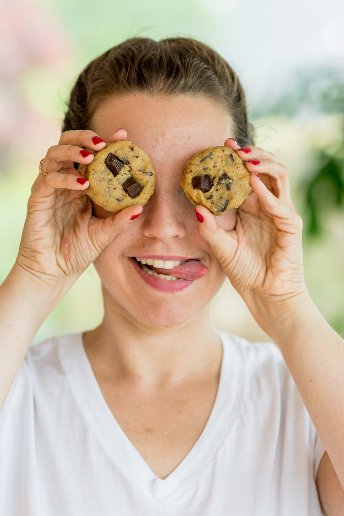 Foto von einer jungen Frau, die sich die Augen mit zwei Chocolate Chip Cookies zuhält.