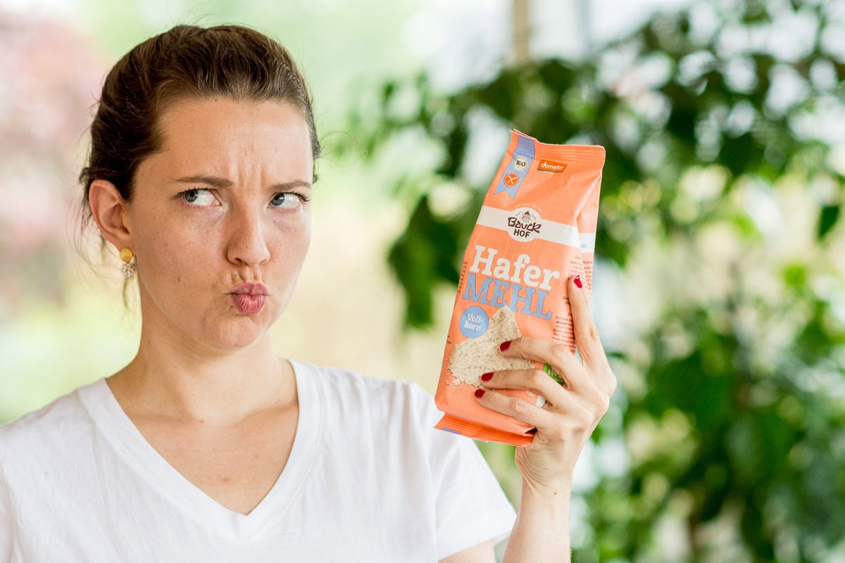 Foto von einer jungen Frau in weißem T-Shirt, die eine Packung Bauckhof Hafermehl in der Hand hält.