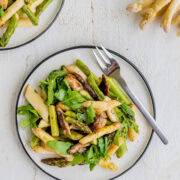 Warmer Spargelsalat mit weißen und grünen Spargelstücken, Shitake-Pilzen und frischem Rucola auf einem Teller.