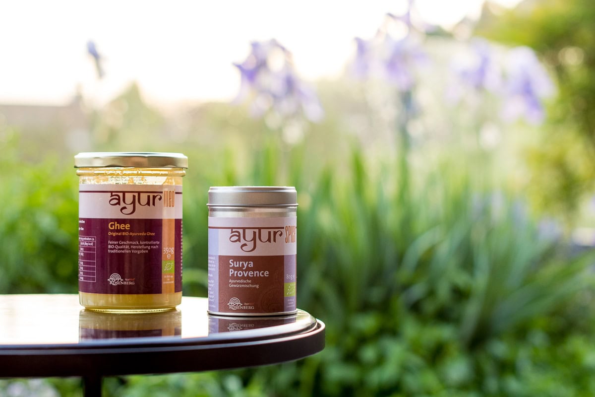 Pinne das Foto, um dir das Rezept für ayurvedisches Ofengemüse zu speichern! Front Shot von einem Glas Ghee und einer Dose Surya Provence Gewürz von Rosenberg AyurMed