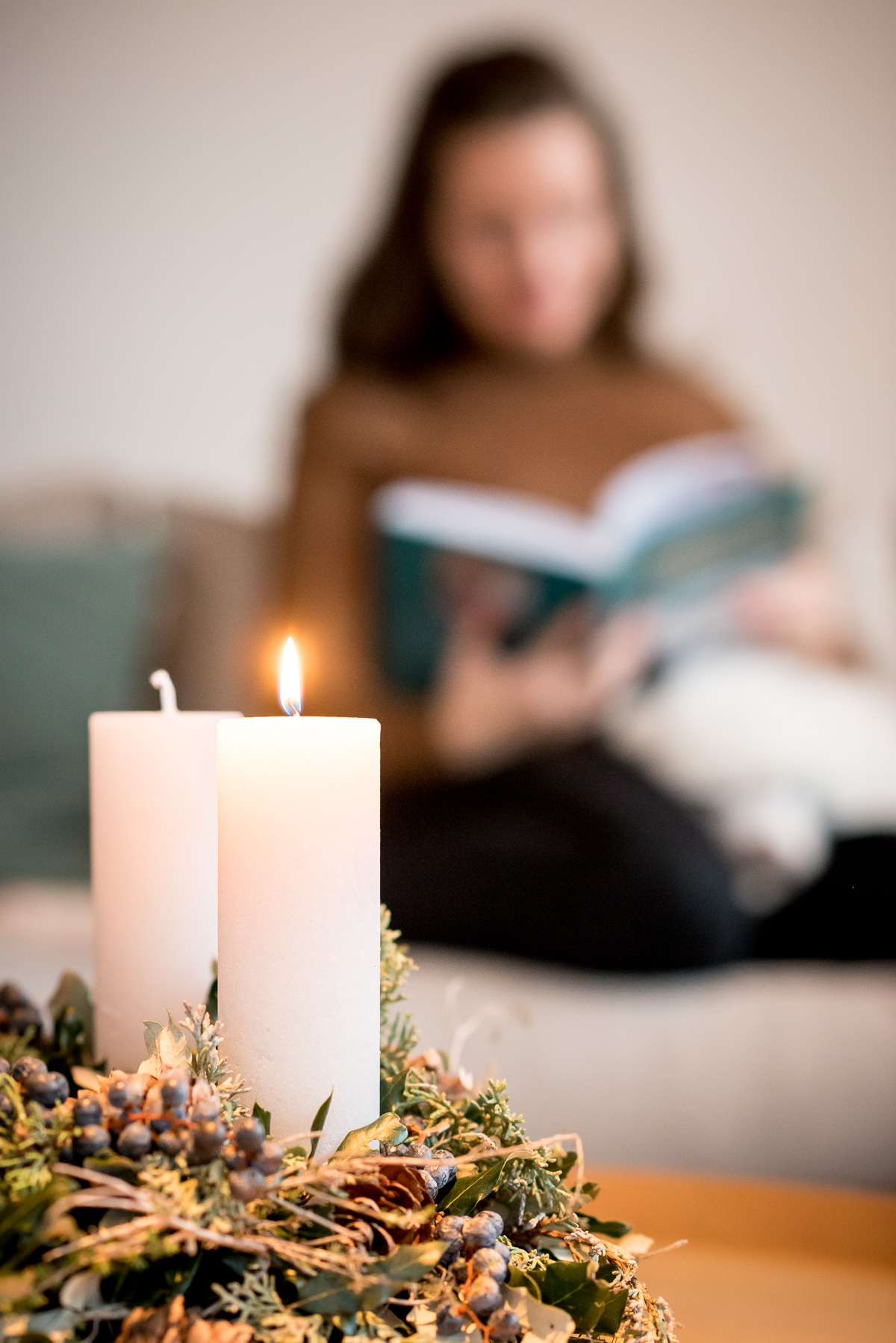 Frau blättert im Buch "Von wilder Welt und Weihnachten", im Vordergrund ein Adventskranz.