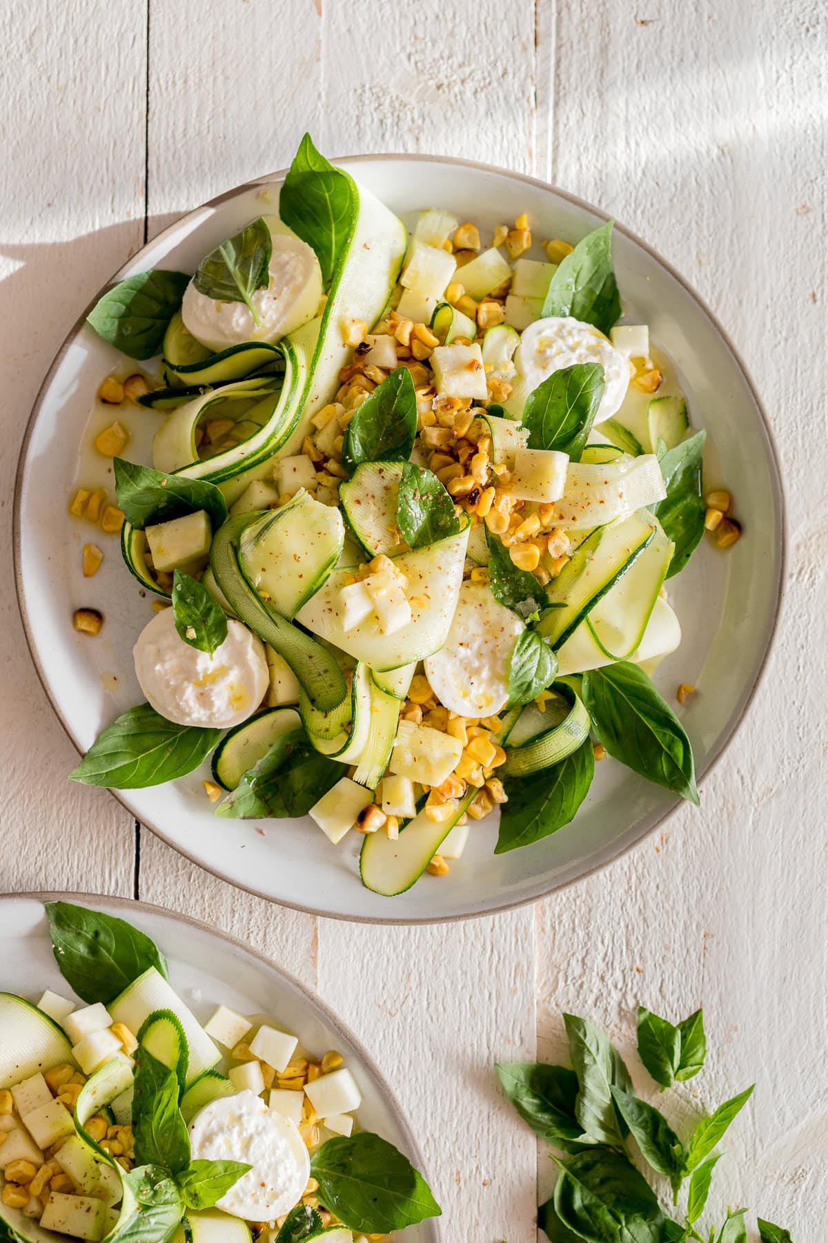 Topshot von sommerlichem Zucchinisalat mit gegrilltem Mais, Basilikum und Mini-Burrata